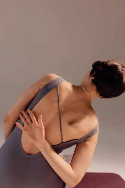 Attractive woman bending body close up. Athletic woman stretches her body on a mat in the studio. A strong muscular sportswoman is engaged in gymnastics on a light background.