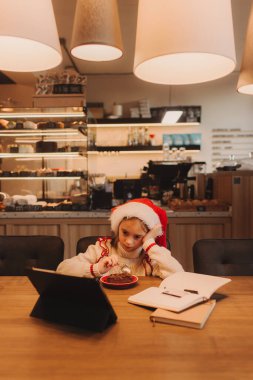 Mutlu kız Noel tatilinin tadını çıkarıyor, kafede tablet iPad 'e bakarken çikolatalı tatlı yiyor..