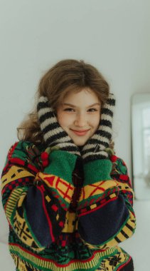 Örgü süveter ve sıcak eldivenlerle gülümseyen neşeli genç kız. Neşeli gülümseyen genç bir kadın Noel tatiline hazırlanıyor. Seçici odak.