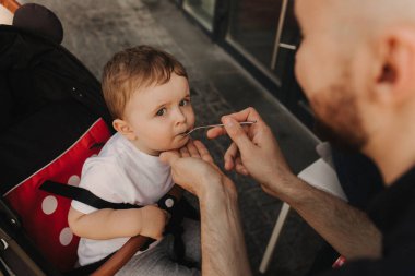 Bir baba küçük oğlunu besler. Çocuk yiyor ve kameraya bakıyor. Bebek maması konsepti. Yumuşak odak bulanık ve gürültü efekti.