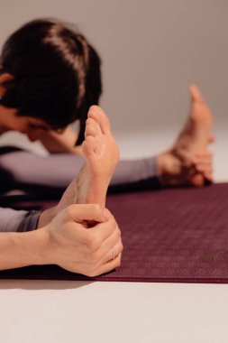 Atletik kadın stüdyoda bir paspasın üzerine uzanıyor. Hafif bir arka planda otururken yoga yapan bir kadının yakın plan bacakları.