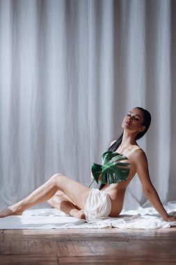 Vücudunu bez ve yeşil yaprakla kaplayan ince vücutlu güzel bir genç kadının portresi. Kendini sevmek. Güzellik, tarz, moda, kozmetoloji, vücut ve cilt bakımı, spor, reklam.