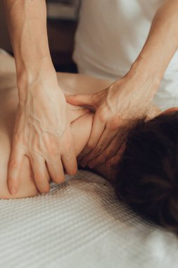 Masaj masasında yatan genç bir kadının omuzlarına masaj yapan kadın masörlerin elleri. Fizik tedavi konsepti, boyun basınç noktası..