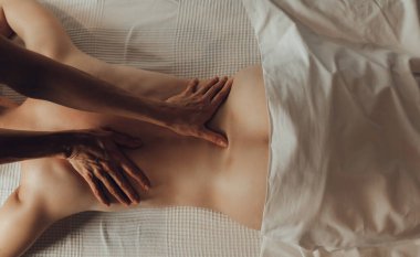 Masaj masasında beyaz arka planda yatan genç bir kadına masaj yapan kadın kayropraktik uzmanının elleri. İçsel masaj. Fizik tedavi konsepti, boyun basınç noktası..