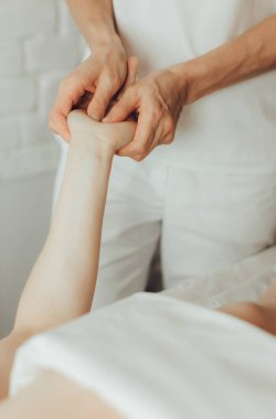 Masaj masasında beyaz arka planda yatan genç bir kadının avuç içi masajı yapan kadın kayropraktik uzmanının elleri. Fizik tedavi konsepti, boyun basınç noktası..