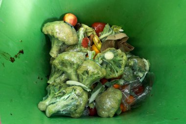 Top view of garbage can with of rotting broccoli in plastic packaging. clipart