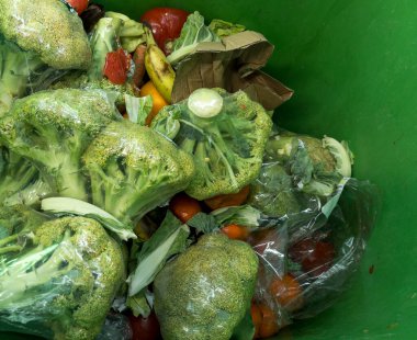 Plastik ambalajında çürüyen brokoli bulunan çöp kutusunun üst görüntüsü.