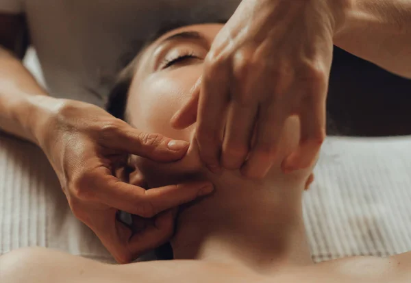 Hands of female chiropractor massaging face of young woman lying on massage table. Visceral massage. Concept of physical therapy treatment, neck pressure point.