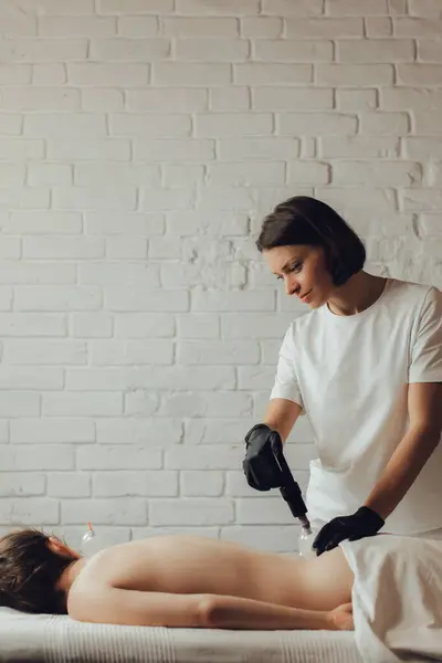 Hands of female chiropractor massaging back of young woman lying on massage table. Masseuse applying vacuum cup on loin of client. Concept of physical therapy treatment, neck pressure point.