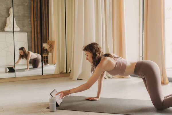 Live streaming on a smartphone - online yoga lesson. Beautiful woman training at home and watching online lessons in the digital tablet. Vintage tonned. Soft focus blurred and noise effect.