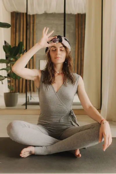 Woman practicing yoga and meditation at home sitting in lotus pose on yoga mat, relaxed with closed eyes. Mindful meditation concept. Wellbeing. No focus blurred and noise effect.
