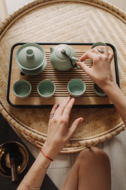 Genç bayan çay seremonisi hazırlıyor. Kadın elleri bardakları tutuyor. Geleneksel Çin çay seremonisi aksesuarları ve çay fincanları olan ahşap masa. Yumuşak odak, bulanık ve gürültü efekti.