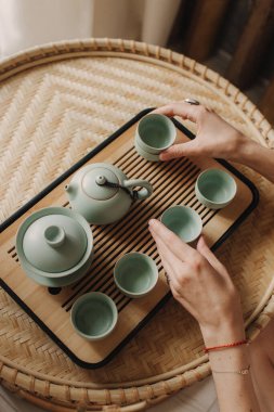 Genç bayan çay seremonisi hazırlıyor. Kadın elleri bardakları tutuyor. Geleneksel Çin çay seremonisi aksesuarları ve çay fincanları olan ahşap masa. Yumuşak odak, bulanık ve gürültü efekti.
