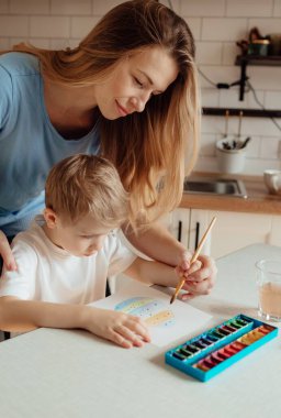 Paskalya için hazırlanıyorum. Aile evde. Paskalya Ailesi gelenekleri. Sevgi dolu bir anne ve küçük mutlu bir çocuk evdeki rahat aydınlık mutfakta gülümseyen neşeli bir kart çizer..