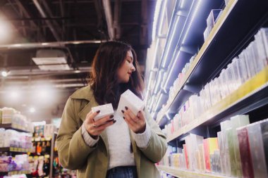 Perakende mağazasından alışveriş yapan genç bir kız. Güzeller güzeli gençlik testleri ve kozmetik ürünleri bir güzellik mağazasından almak. Yan görüş. Kişisel bakım ve modern kozmetoloji. Güzellik ve moda. Perakende ve tüketim.