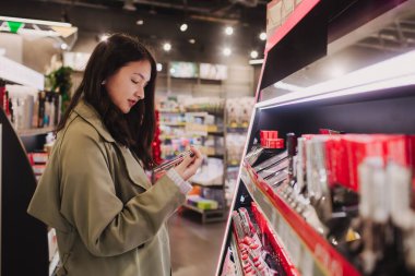Güzeller güzeli gençlik testleri ve kozmetik ürünleri bir güzellik mağazasından almak. Kozmetik mağazasında ruj deneyen genç bir kız. Perakende ve tüketim. Kişisel bakım ve modern kozmetoloji. Yan görünüm.