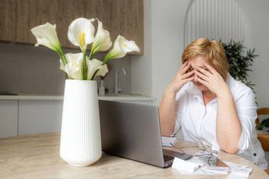 Üst düzey iş kadını elinde dizüstü bilgisayarla kağıt para tutuyor. Yaşlı kadın banka hesaplarını yönetiyor, bütçe vergilerini hesaplıyor, banka borçları için emeklilik ödemelerini planlıyor mutfak masasında oturuyor..