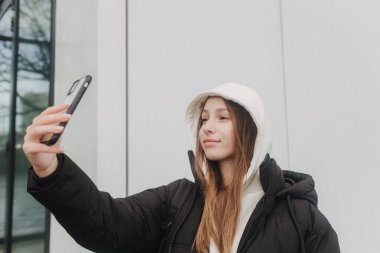 Güz-kış sezonunda şehirde blog yazmak için günlük kıyafetli bir kızın yarım boy portresi. Açık havada internette sörf yapan gençler..