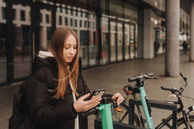 Okul çağındaki bir kız akıllı telefon kullanarak elektrikli scooter ya da bisiklet kiralıyor. Cep telefonu uygulaması ile ulaşılamaz ödemeler yapıyor. Sonbahar-kış sezonunda şehirde bisiklet kiralama.