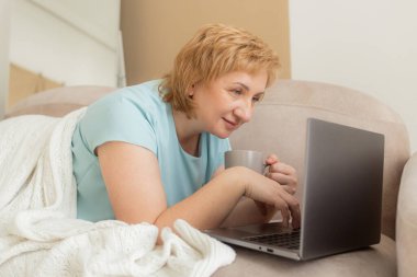 Gülümseyen son sınıf öğrencisi kadın evde dinleniyor dizüstü bilgisayar kullanıyor video veya film izliyor teknolojiden, boş zamanlardan, emeklilik yaşam tarzından keyif alıyor..