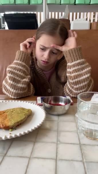 朝食を食べながら携帯電話を使っている美しい女の子 カフェで食べ物を食べながらビデオゲームをしているかわいい10代の少女 リアルタイム映像 ジェネレーションアルファ — ストック動画