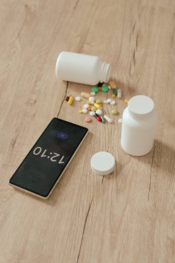 Farklı haplar ve ahşap bir masadaki telefonun çalar saati. Tıp ve sağlık hizmetleri kavramı. Bir serinin parçası.