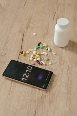 Farklı haplar ve ahşap bir masadaki telefonun çalar saati. Tıp ve sağlık hizmetleri kavramı. Bir serinin parçası.