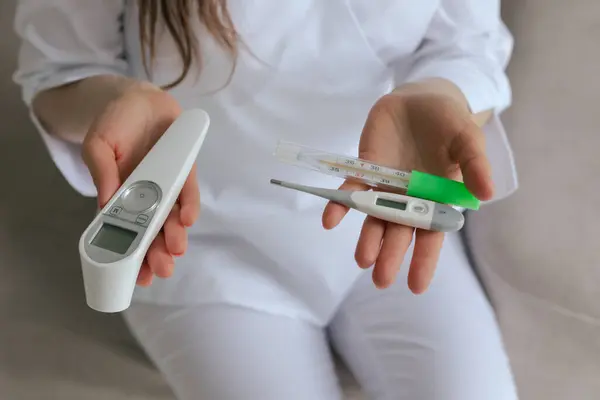 stock image Close-up female gp physician doctor holding different types of thermometers for measuring human body temperature - mercury, infrared, electronic. Concept of medicine and healthcare. Part of a series.