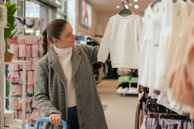 Dükkanda bebek kıyafetleri ya da çocuk kıyafetleri seçen genç müşteri. Küçük çocuklar için mağazadan alışveriş yapmak..