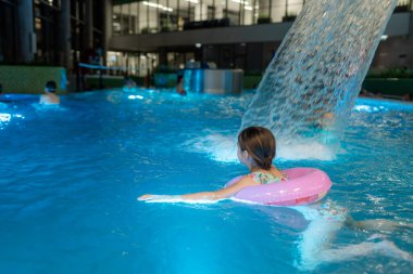 Kapalı bir spor havuzunda yüzen ve şifalı sularda yüzen küçük şirin bir kızın yakın plan portresi. Mutlu çocuk suda, yaz tatilinde ve tatil konseptinde eğleniyor. Boşluğu kopyala.