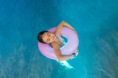 Kapalı bir spor havuzunda yüzen ve şifalı sularda yüzen küçük şirin bir kızın yakın plan portresi. Mutlu çocuk suda, yaz tatilinde ve tatil konseptinde eğleniyor. Boşluğu kopyala.