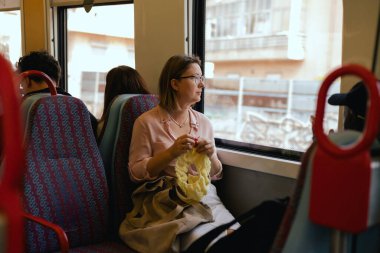 Toplu taşımacılıkta yün kullanarak örgü işi yapan çekici bir kadın. Zamanda yolculuğun tadını çıkaran rahat bir kadın. Seyahat konsepti üzerinde yaratıcı aktiviteler. Uzayı kopyala Dizinin bir parçası.