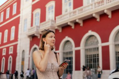 Şehir yolculuğu konsepti. Telefonundaki bilete bakan ve istasyonda ulaşımı bekleyen turist kadın, başvuru formunda internetten bilet ayırtıyor. Uzayı kopyala Dizinin bir parçası.