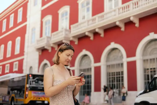 stock image City travel concept. Tourist Woman looking at a ticket on her phone and waiting for transport at station, passenger books a ticket online through in the application. Copy space. Part of the series.