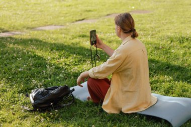 İletişim için orta yaşlı kadın, telefon ve iletişim ağı, sosyal medya ve yaz parkında haber uygulaması. Yoga minderinde otururken selfie çeken bir kadın. Doğayla birlik, spor yoga konsepti.