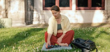 İletişim, sosyal medya ve yaz parkında haber uygulamaları için telefon ve iletişim ağı olan orta yaşlı bir kadın. Yoga minderinde oturan kadın. Doğayla birlik, spor yoga konsepti.