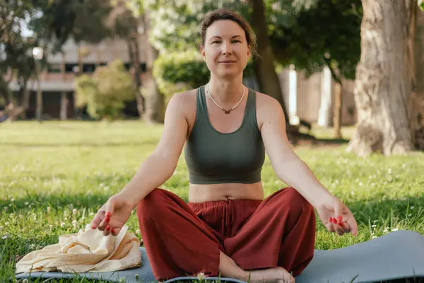 stock image Middle aged woman practicing breathing yoga pranayama outdoors. Yoga instructor doing yoga exercise in the park, sport yoga concept. Unity with nature concept.