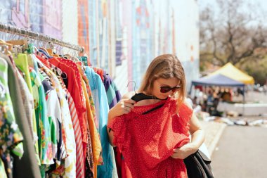 40 'lı yaşlarda bitpazarından kırmızı elbise alan doğal görünümlü bir kadının portresi. Garaj satışı, giysileri tekrar kullanma, ikinci el ve ekolojik tüketici. Solo turizm