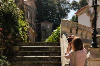 Gözlem güvertesindeki orta yaşlı gezgin kadın, Portekiz 'deki Quinta da Regaleira şehrinin güzel bir manzarasıyla fotoğraf çekiyor. Seyahat ve solo turizm konsepti. Dizinin bir parçası.