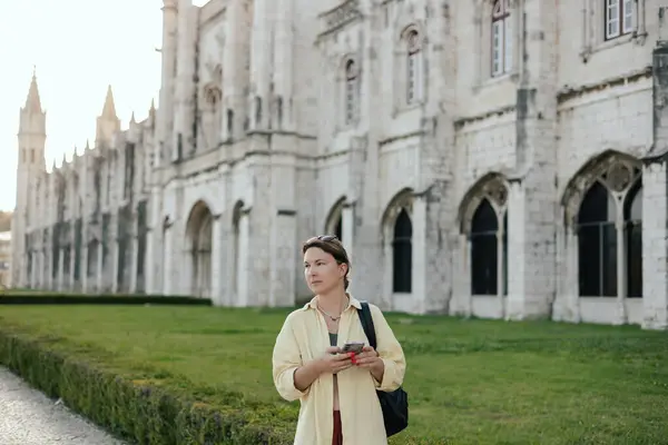 Stock image Middle aged traveling woman looks for the way using the online map on her phone and passes the Monteiro dos Jeronimo's in Belem, Lisbon, Portugal. Travel and solo tourism concept. Part of the series.