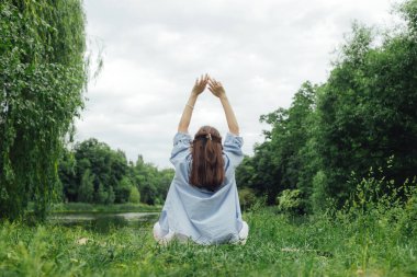 Koreli kız parkta yoga meditasyonu yapmak için ellerini gökyüzüne uzatıyor. Doğayla bütünlük ve refah kavramı. Dizinin bir parçası