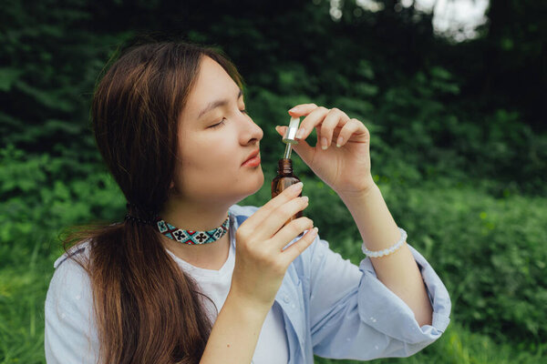 Корейская девушка с флаконом с эфирным маслом в парке. Единство с природой и концепция wellness. Часть серии ". Концепция средства по уходу за волосами на концах волос или защита от солнца.