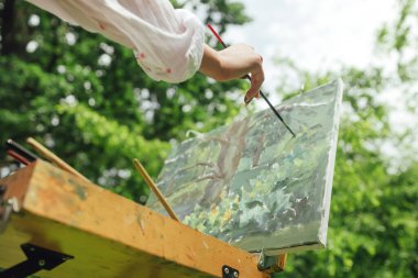 Kadın sanatçıların ellerini kapatarak tuvale fırça darbesi vurun. Farkındalık, sanat terapisi, yaratıcılık kavramı. Doğada plein hava boyama işlemi. Dizinin bir parçası