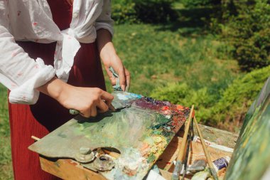 Kadın sanatçının ellerini yakın çekimde sehpadaki boya paletini temizleyin. Farkındalık, sanat terapisi, yaratıcılık kavramı. Doğada plein hava boyama işlemi. Dizinin bir parçası.