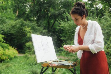 Kadın sanatçılar parkta bir resim çizerler. Farkındalık, sanat terapisi, yaratıcılık kavramı. Doğada plein hava boyama işlemi. Bir tablonun adım adım oluşturulmasını gösteren bir dizi fotoğraf.
