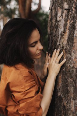 Açık hava eğlence parkında mutlu yetişkin kadın ağaç gövdesine sarılıyor. Çevre ve çevre bakımı kavramı. İnsanlar Dünya gezegenini sever ve ormanların yok oluşunu durdurur.
