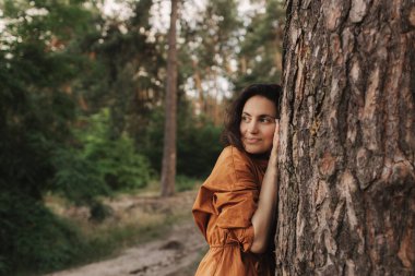 Açık hava eğlence parkında mutlu yetişkin kadın ağaç gövdesine sarılıyor. Çevre ve çevre bakımı kavramı. İnsanlar Dünya gezegenini sever ve ormanların yok oluşunu durdurur.