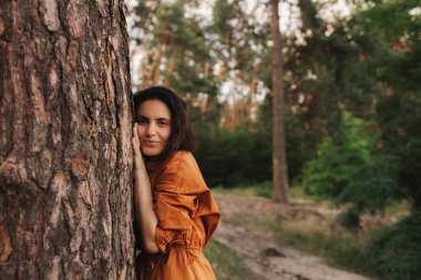 Açık hava eğlence parkında mutlu yetişkin kadın ağaç gövdesine sarılıyor. Çevre ve çevre bakımı kavramı. İnsanlar Dünya gezegenini sever ve ormanların yok oluşunu durdurur.