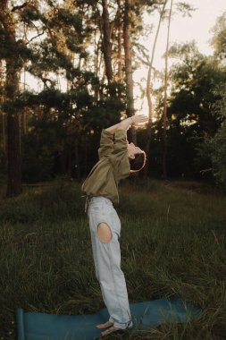 Doğayla bütünlük ve refah kavramı. Yoga antrenmanı için yoga minderiyle eğlenen aşırı neşeli kadın parkta meditasyon yapıyor. Kadın insan kavramı ve sağlıklı doğal yaşam tarzı. Dizinin bir parçası.