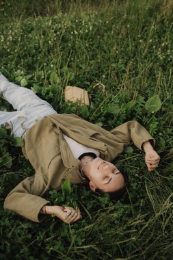 Güzel, sevimli bir kadın. Beyaz gömlekli, beyaz çiçekli yeşil çimlerin üzerine uzanmış makyajı yok. Vahşi doğa, ruh hali tatili, rahatlama. En iyi kız manzarası. Özgür ol, aşk ormanı. Dizinin bir parçası.